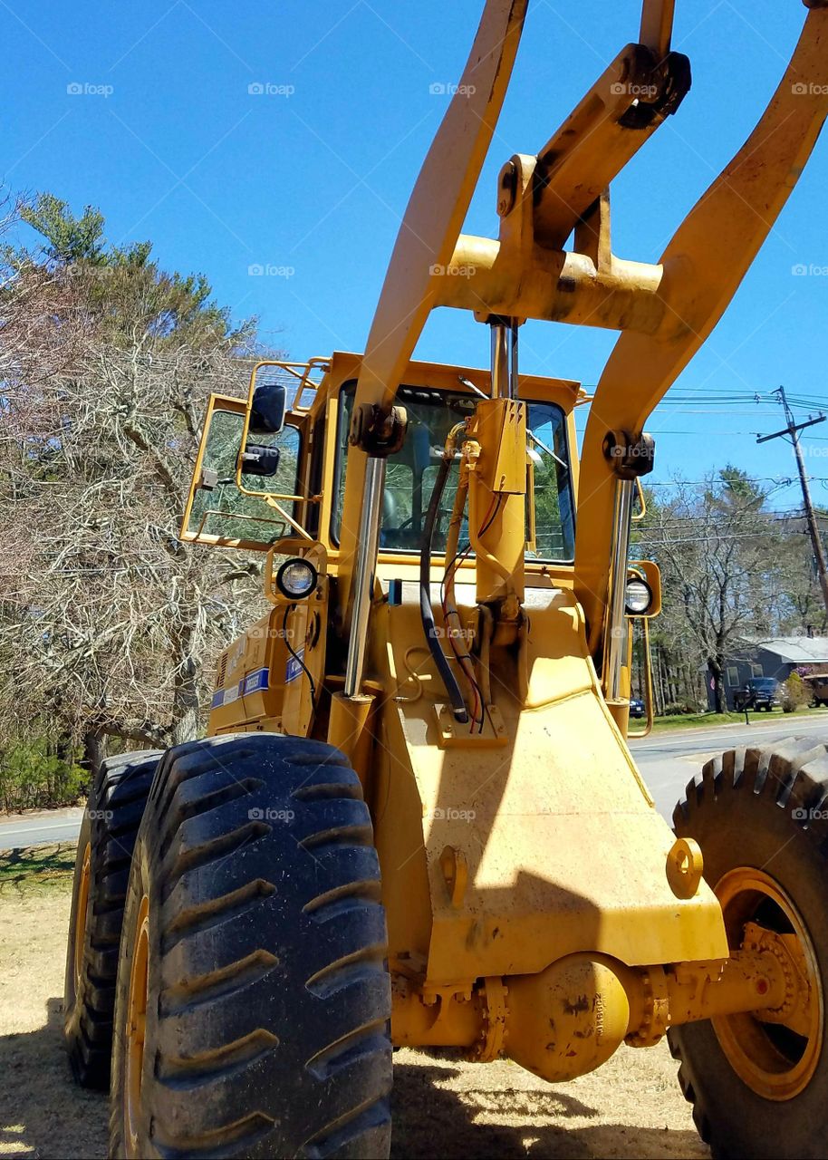 Front End Loader in yard with bucket high, out of sight. Bucket reaching high in air.🚜 Blue sky, street roadway in background. Working in yard with heavy equipment.