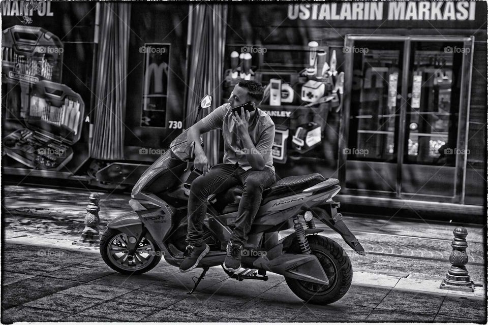 man sitting on motorcycle talking on mobile Istanbul Turkey. street photography monochrome