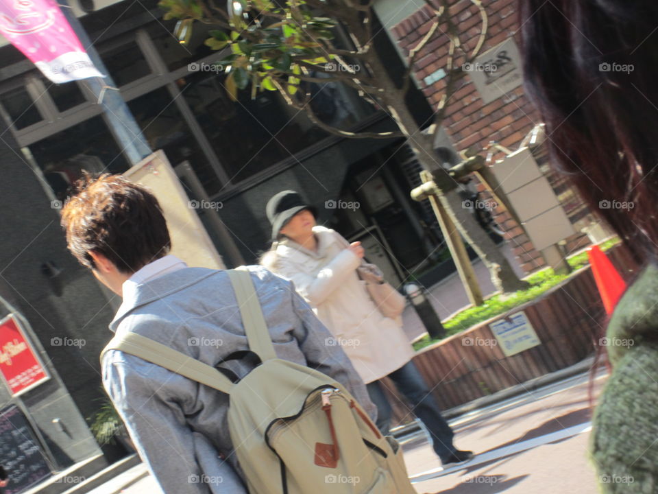 Elderly Lady in Hat and Young Man with Backpack Walk Down a Street in Tokyo, Japan, in Opposite Directions