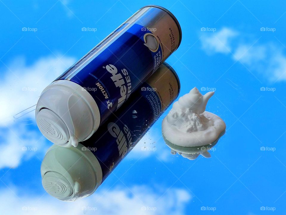 Shaving foam.  On the mirror surface there is white shaving foam and a bottle of "Gillette series".  A blue sky with white clouds reflects off a mirror surface