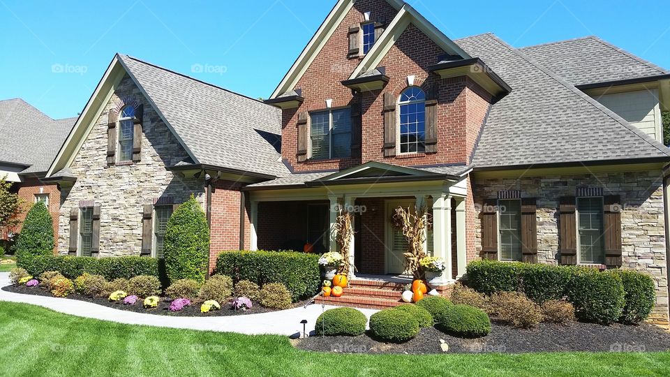 Brick and Stack Stone suburban home with green grass and fall decorations and landscaping