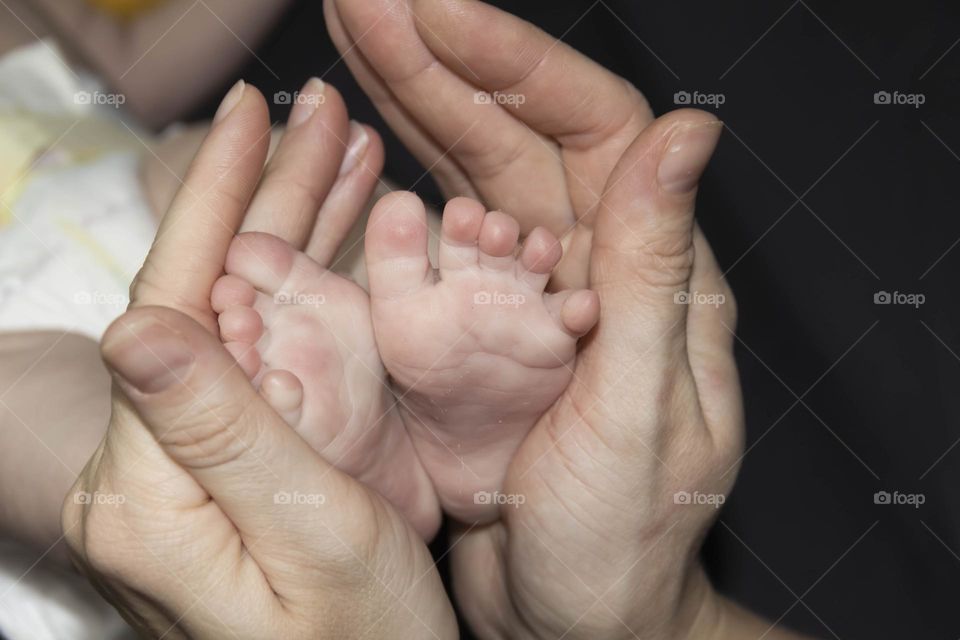 A happy mother in white holds the legs of a newborn baby in her hands. Lifestyle and newborn.
