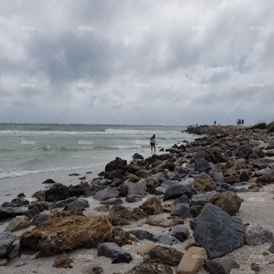 Woman collecting seashells on a rocky beach with dark clouds from the storm coming into Pass-a-Grill, Florida