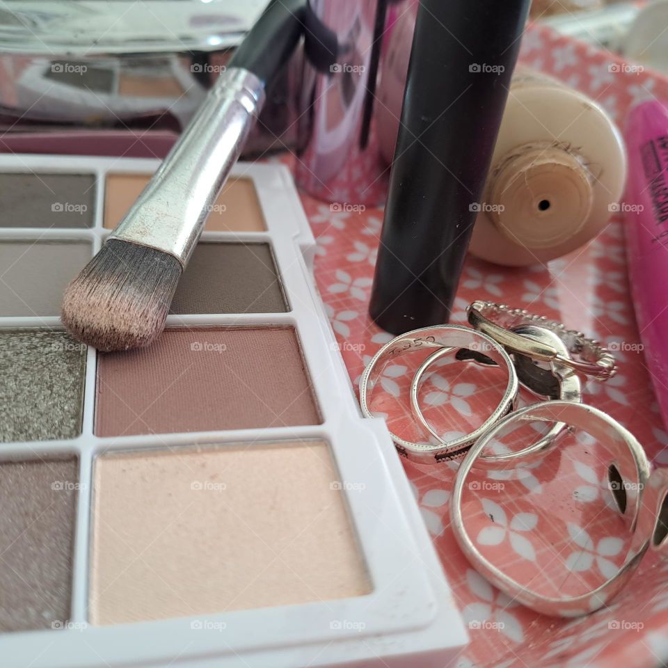 close up pf makeup on a pink tray with rings eyeshadow pallette foundation ladies