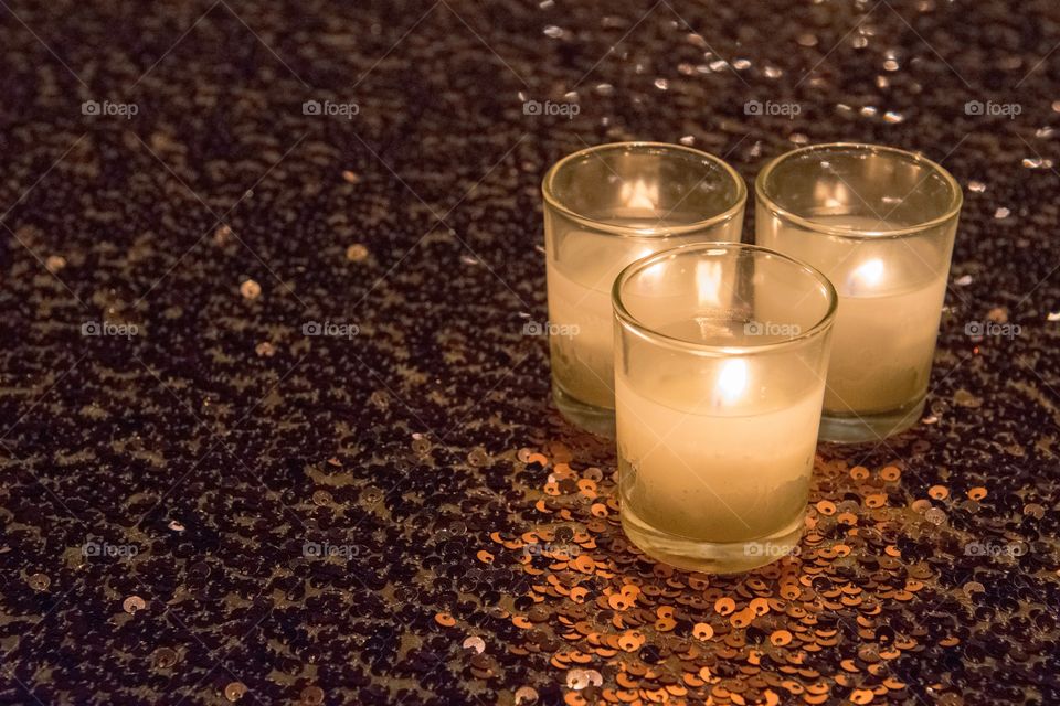 Three tea light candles bunches to the right on a glittery, sequined, tabletop background at a festive occasion.