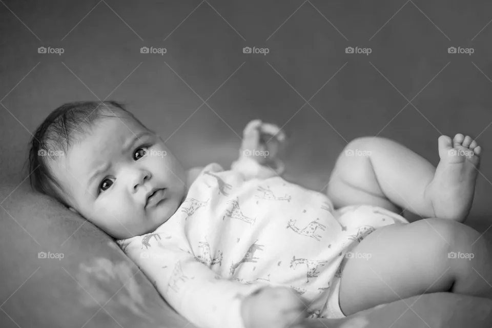 Dramatic photo of a baby lying down, staring right into the camera with her intentional eyes while her foot springs up for a perfect pose. 