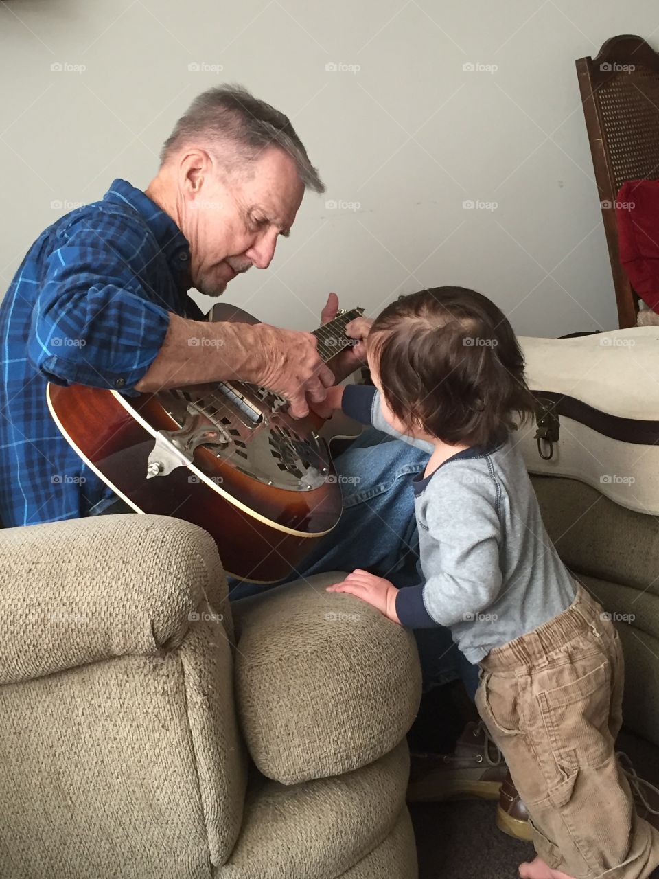 Papa playing a guitar and song for his grandson who is captivated by it. 