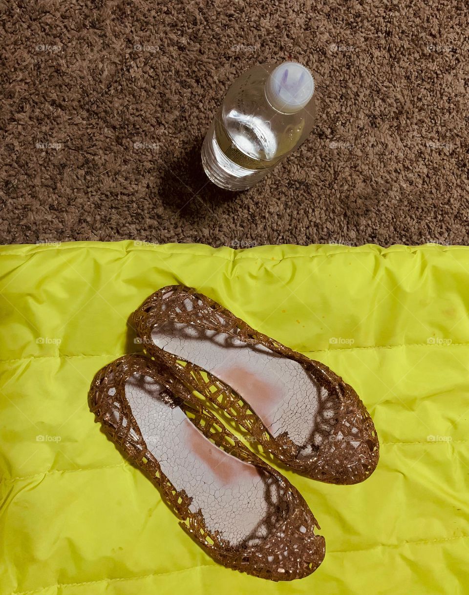 Things I always bring with me in a road trip or anywhere, definitely my sandals shoes sitting on the green blanket and the water bottle on the carpet.