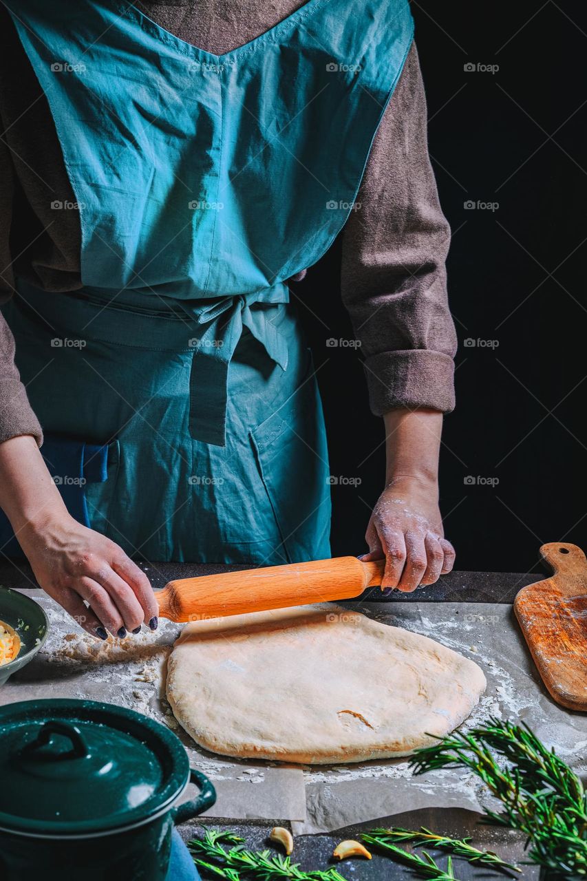 Women's hands, flour and dough. Levitation in a frame of dough and flour. A woman in an apron is preparing dough for home baking. Rustic style photo. Wooden table, wheat ears and flou.Emotional photo