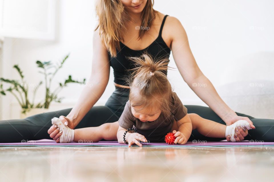 Young woman fit mom with baby girl doing fitness on mat at home