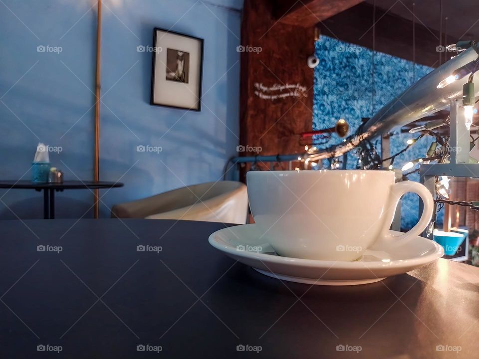 Cup of coffee on a table in a beautiful cafeteria adorned with tables, paintings and lights.