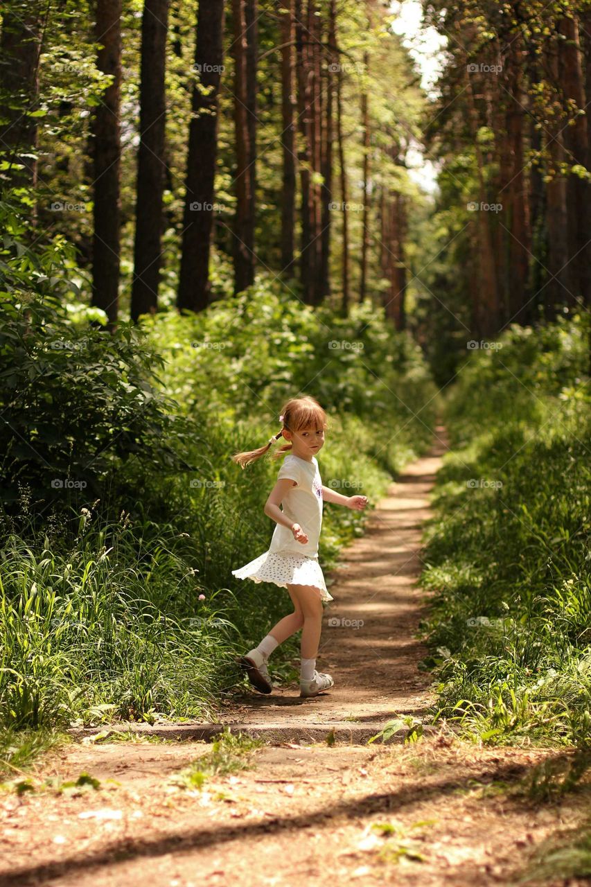 A girl runs along a path between pines in a city botanical garden