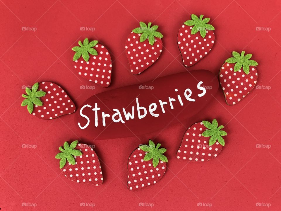 Strawberries conceptual composition with a stone and wooden objects over red background 
