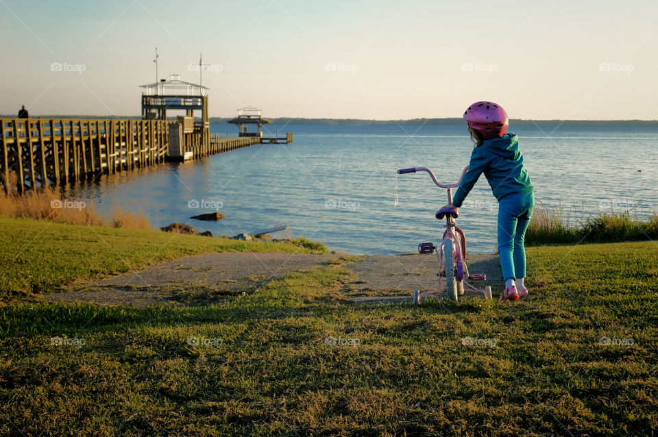 Little girl getting off her bicycle with training wheels at the boat ramp by the pier or dock over the Neuse River estuary in Arapahoe North Carolina. 