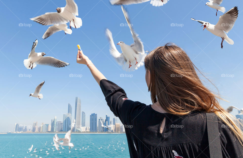 Girl feeding seagulls at the beach looking towards the city