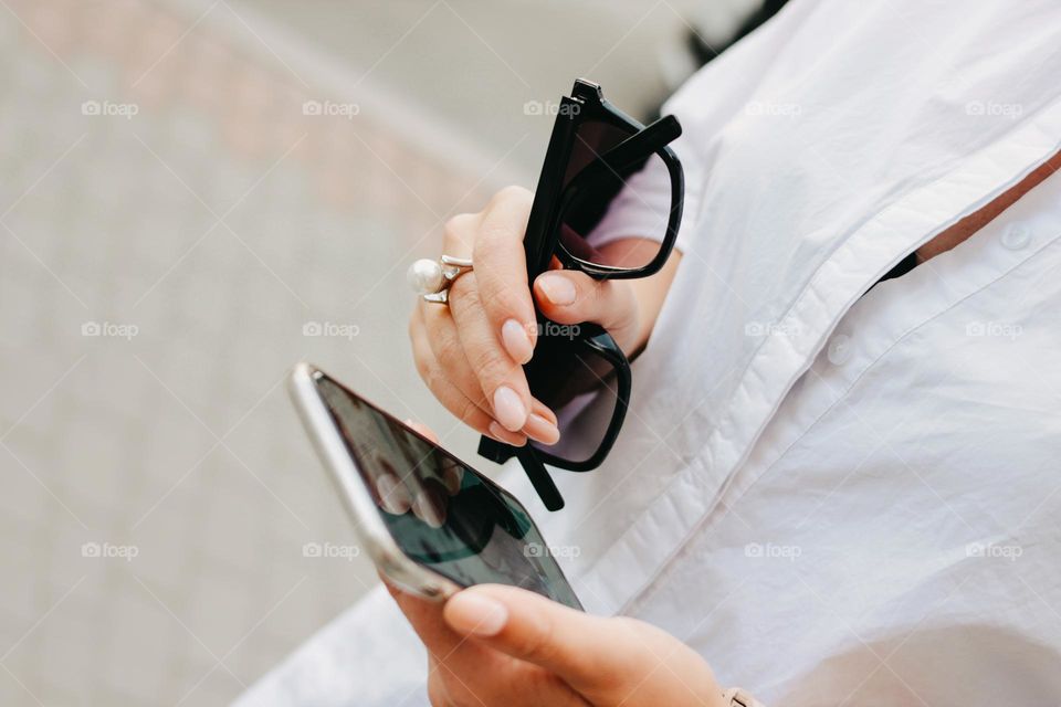 Beautiful successful elegant young woman with sunglasses and mobile phone in her hands, street style