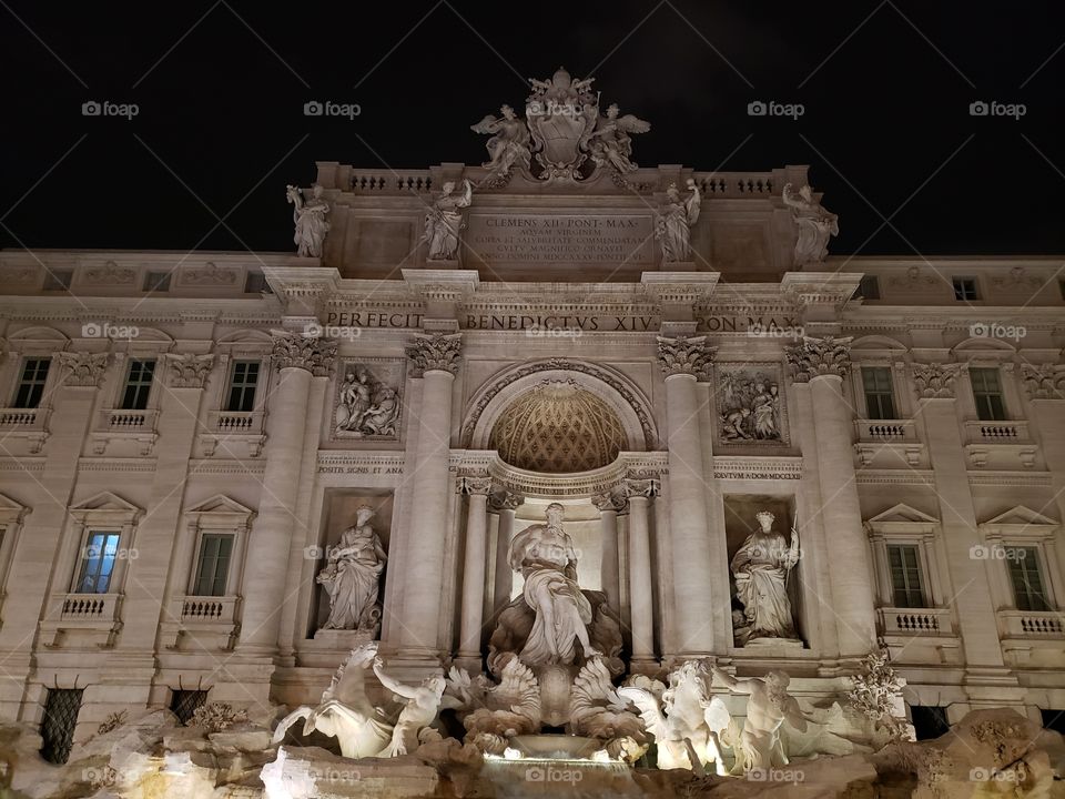 The famous Trevi fountain in Rome, Italy, Europe, in evening time with lights illuminating the statues and water.