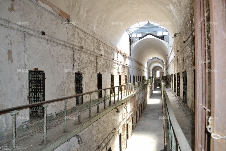A view from the second floor of an abandoned prison corridor with an arched ceiling and metal handrails 