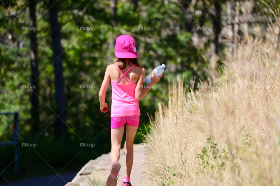 Six year old girl dressed in pink shorts and too, walking across ledge and holding a water bottle 