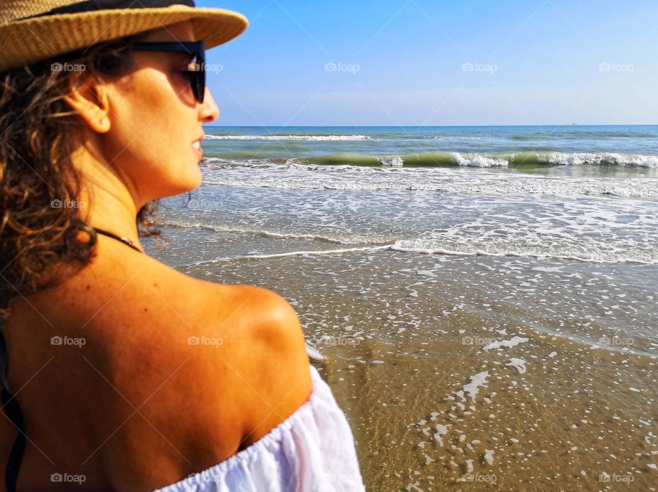 Woman from behind with hat looks at the sea and meditates