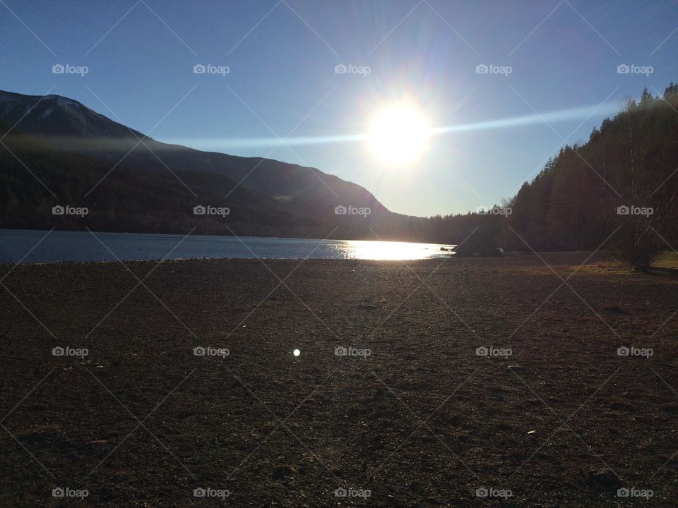 A lake surrounded by a forest with a bright sun above it. The lake is rattlesnake lake in Washington state.