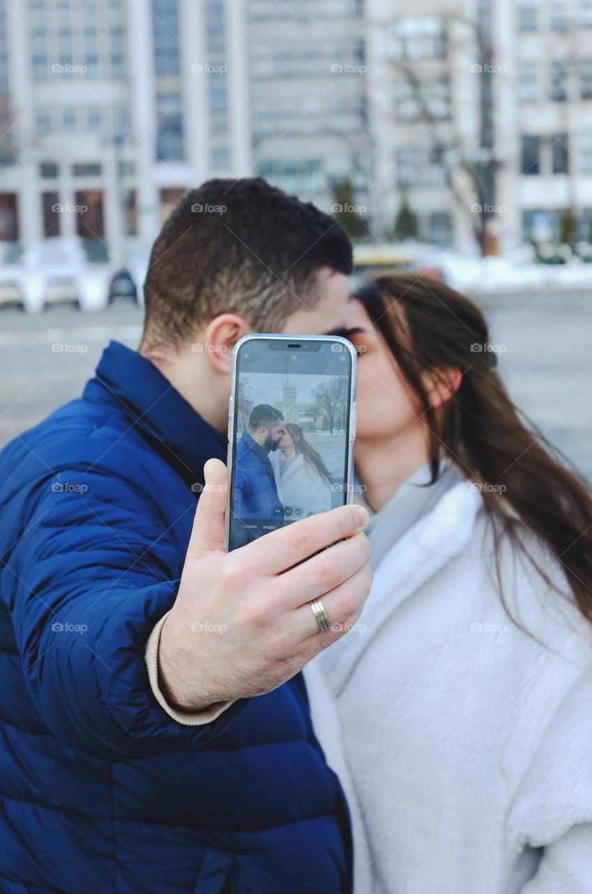 Portrait of young happy couple, bearded man and brunette woman woman relaxing in winter city. Laptop. Phone. Technology. Selfie.  Social media.  Video call