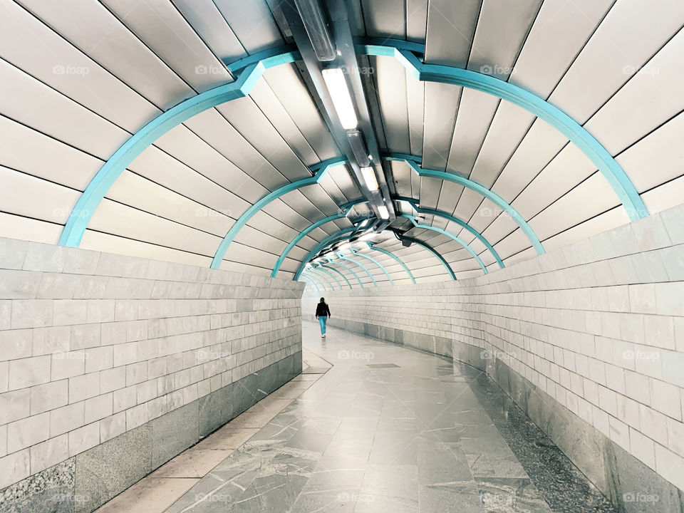 Tiny human walking by the grey and blue tunnel 