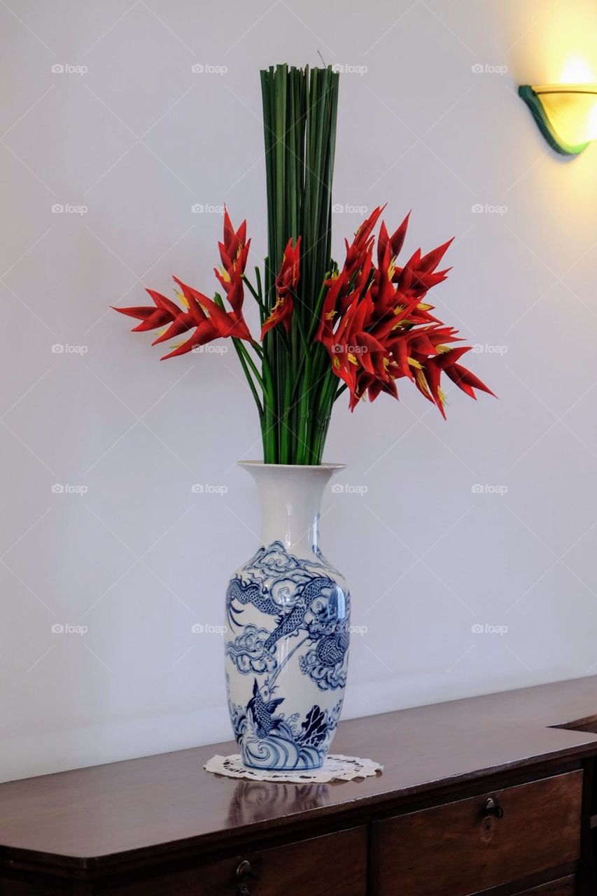 Minimalistic boutique of dark green stems and bright red canna shot arrowroot flowers in Chinese style blue and white vase