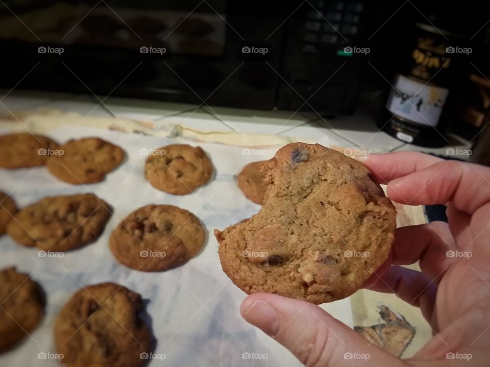 Hand Holding a Fresh Baked Chocolate Chip Cookie with a Bite Taken Out of It.