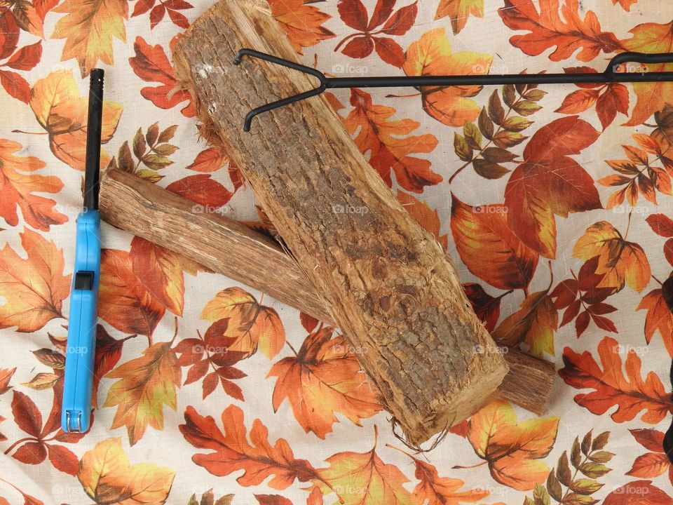 Autumn fall decor and cloth with logs and fire grate closeup with orange drawings of leaves, logs and blue long lighter.