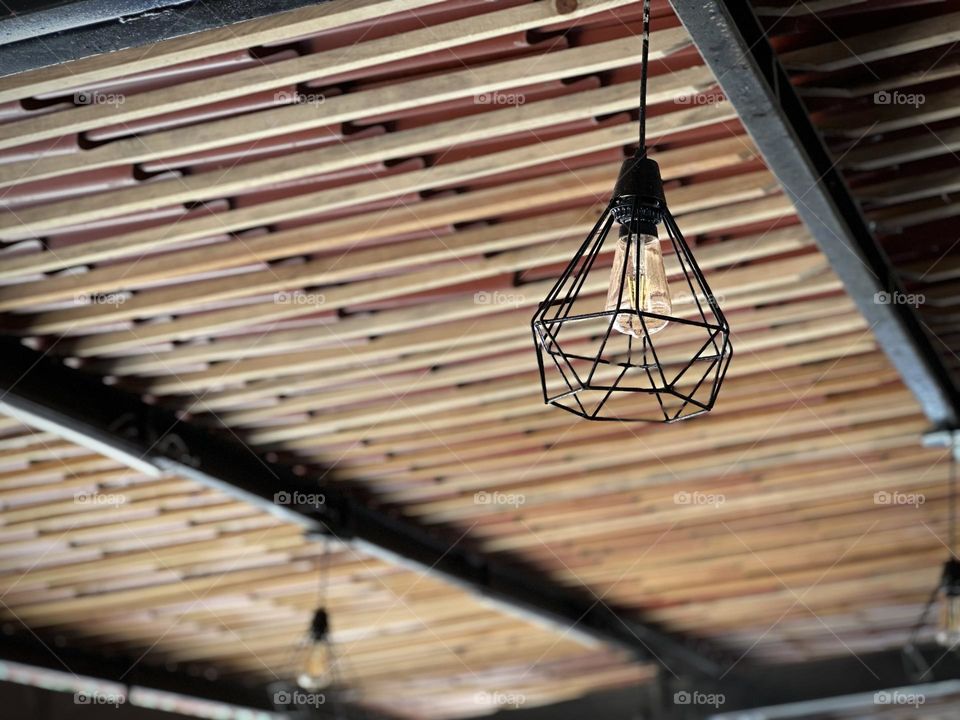 Curious lamp closed-up, inside of a restaurant, with pattern wood sticks on the ceiling.