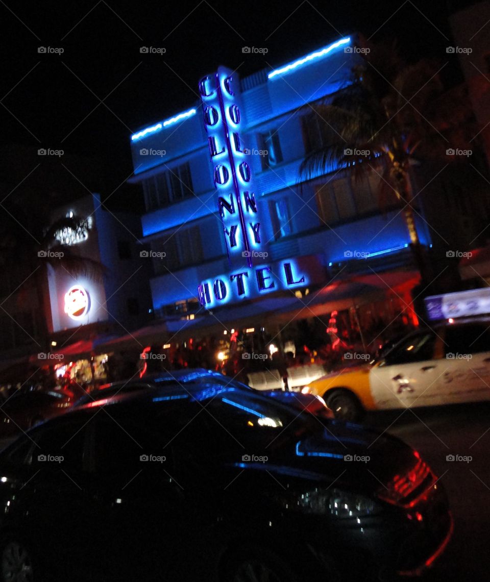 Bright blue lights of the Colony Hotel illuminate Ocean Drive in South Beach on warm winter night.