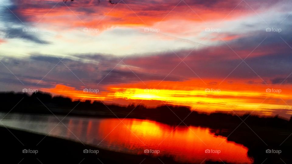 Fiery sunset reflecting bright reds, oranges, yellows, and gray in pond in winter Florida 