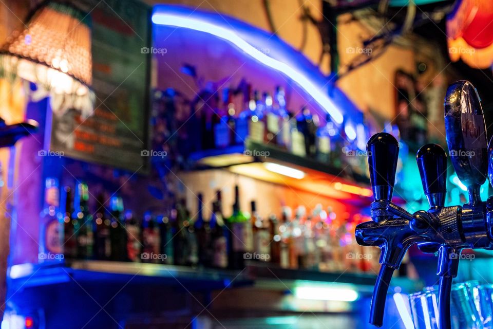 Close-up photo of beer tap in colorful bar with neon lights