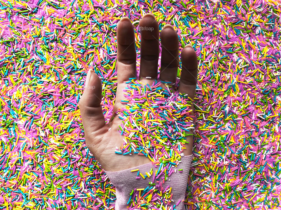 Female hand surrounded by the colorful sweet sprinkles 