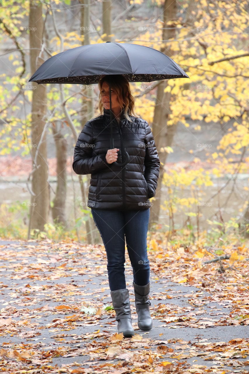Woman walking in rain in Fall holding black umbrella