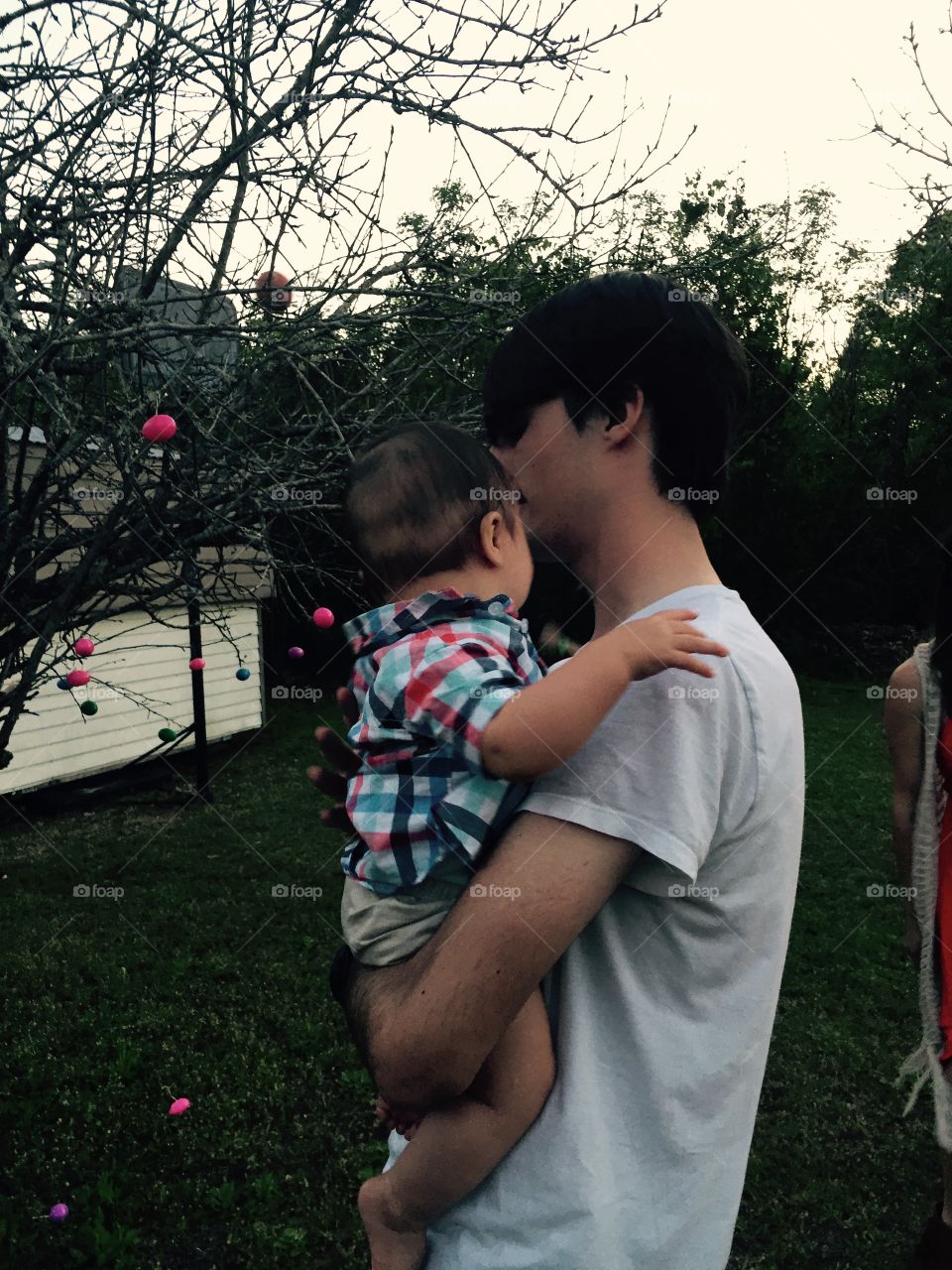 Teenager holding his baby nephew, with their heads turned and both of them in my yard , my grandsons.