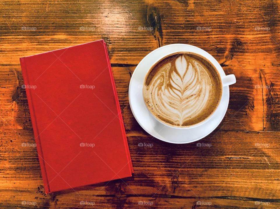 Beautiful coffee art next to a red book on a wooden table for morning breakfast and reading
