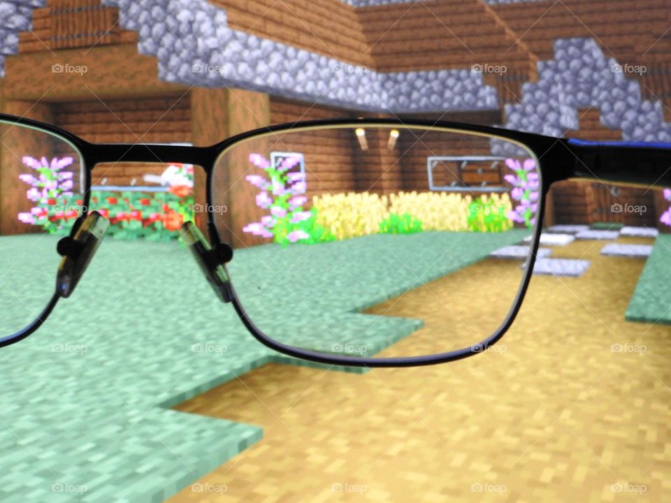 Teenager boy playing Minecraft on the gaming computer seen from his glasses close-up in a dark room.