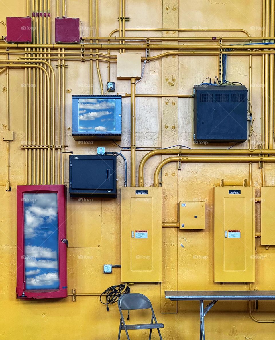 Cloud reflections in the glass doors on electrical control panels against a yellow wall