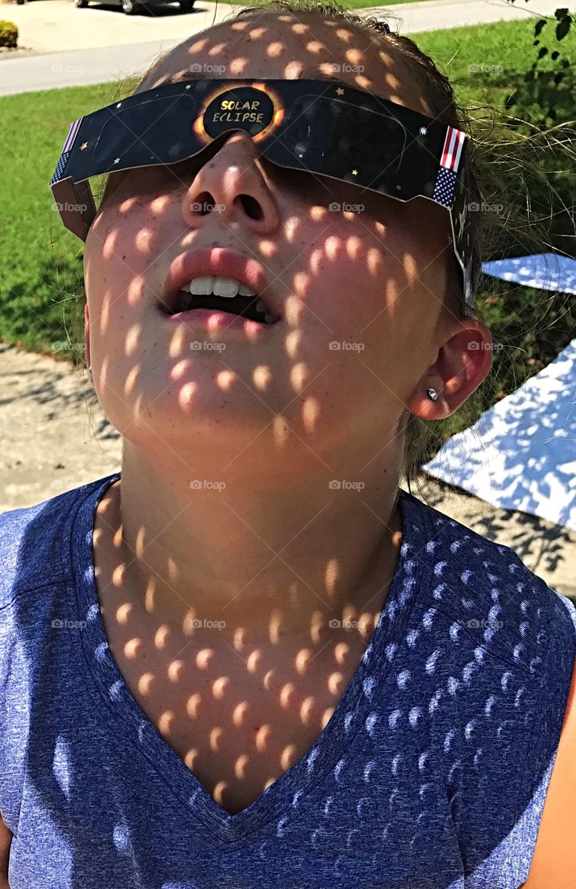 Reflection of solar eclipse through colander on girl watching eclipse through solar glasses