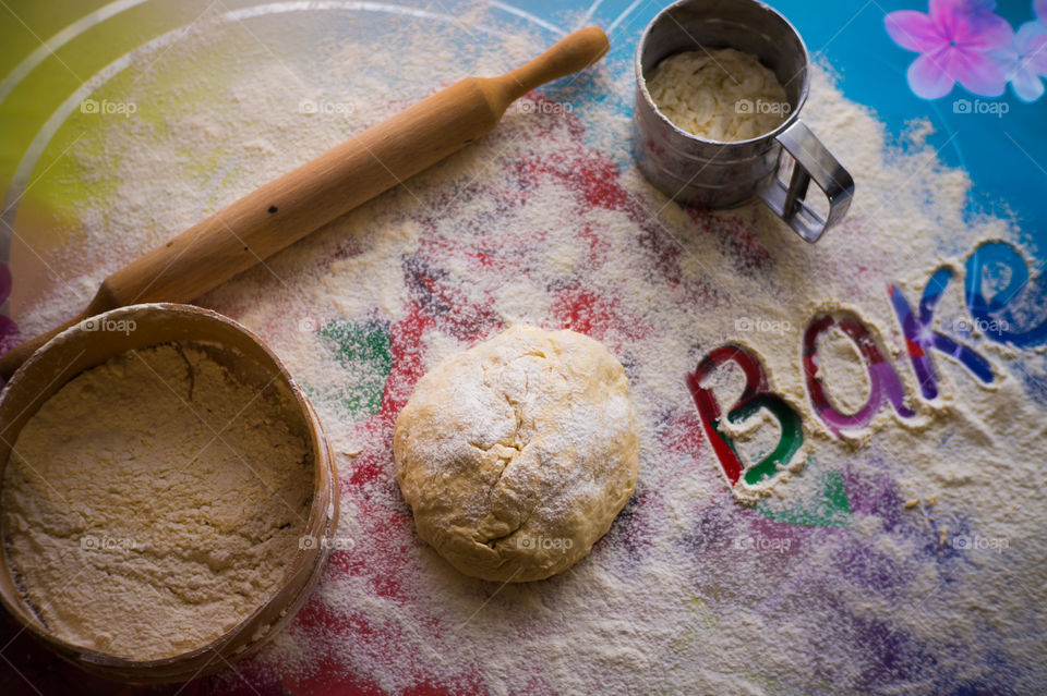 On the table lies a pastry for pies with sprinkled flour and a seeder for flour. Written to bake on the table.