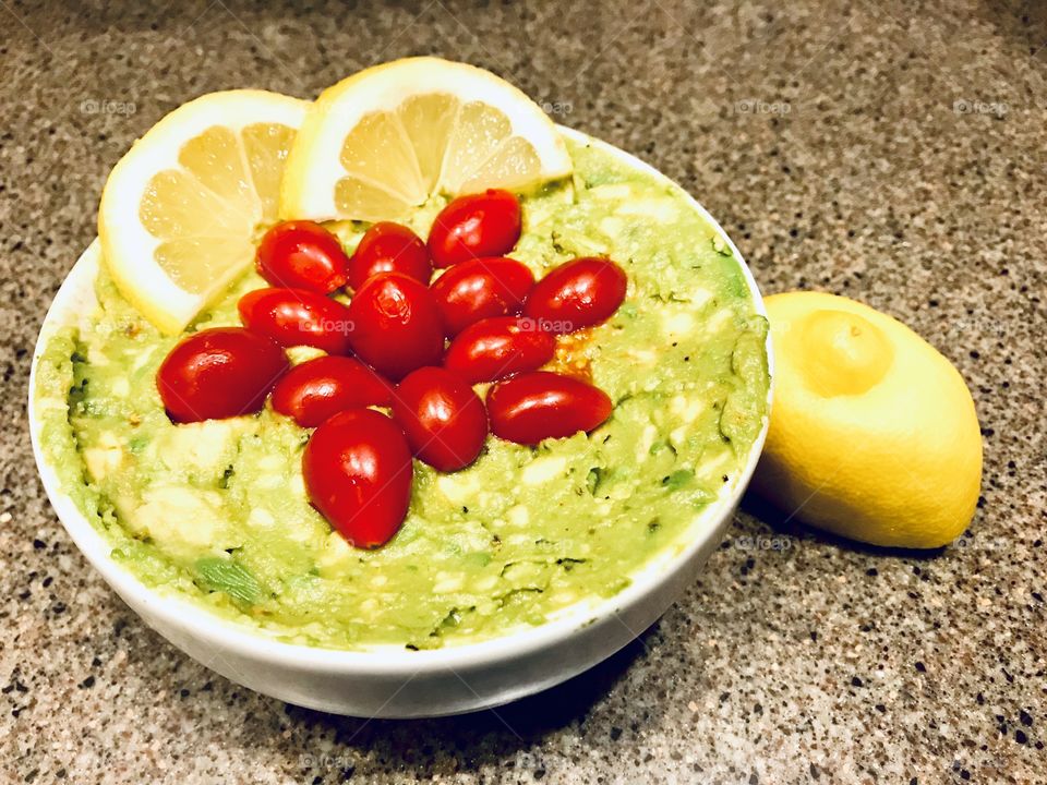 Delicious guacamole with tiny red grape tomatoes and lemon slices made by a child!