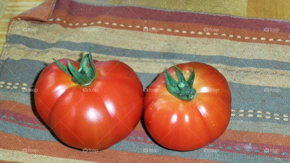 Two bright red orange tomatoes on a colorful striped cloth