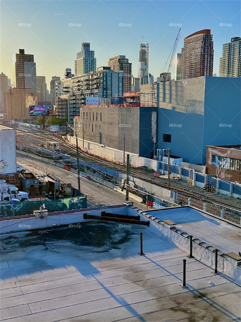 From the staircase of the „Pulaski Bridge“ at „Newtown Creek“ in LIC we overlook the „Long Island Railroad“ and „iFly“, indoor flight simulation in a rectangle building mimicking parachute free fall by upwind propulsion. 2024. Hypnotic Productions