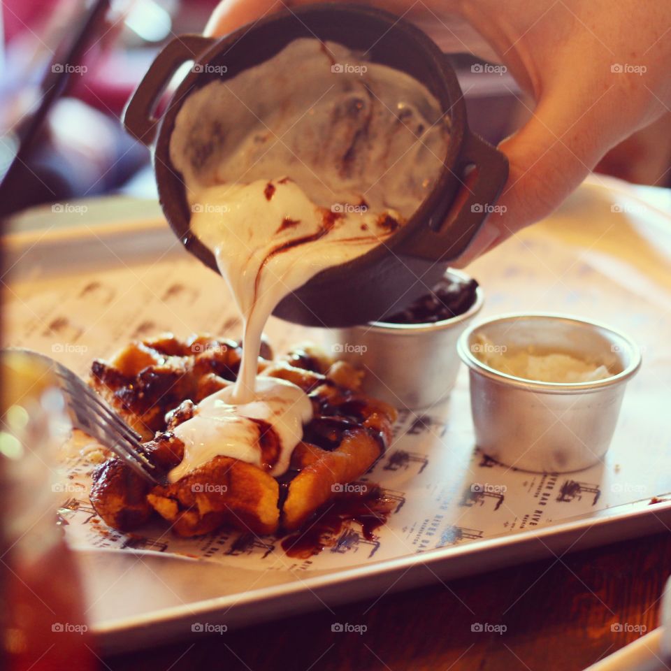 Pouring melted ice cream on waffle. 