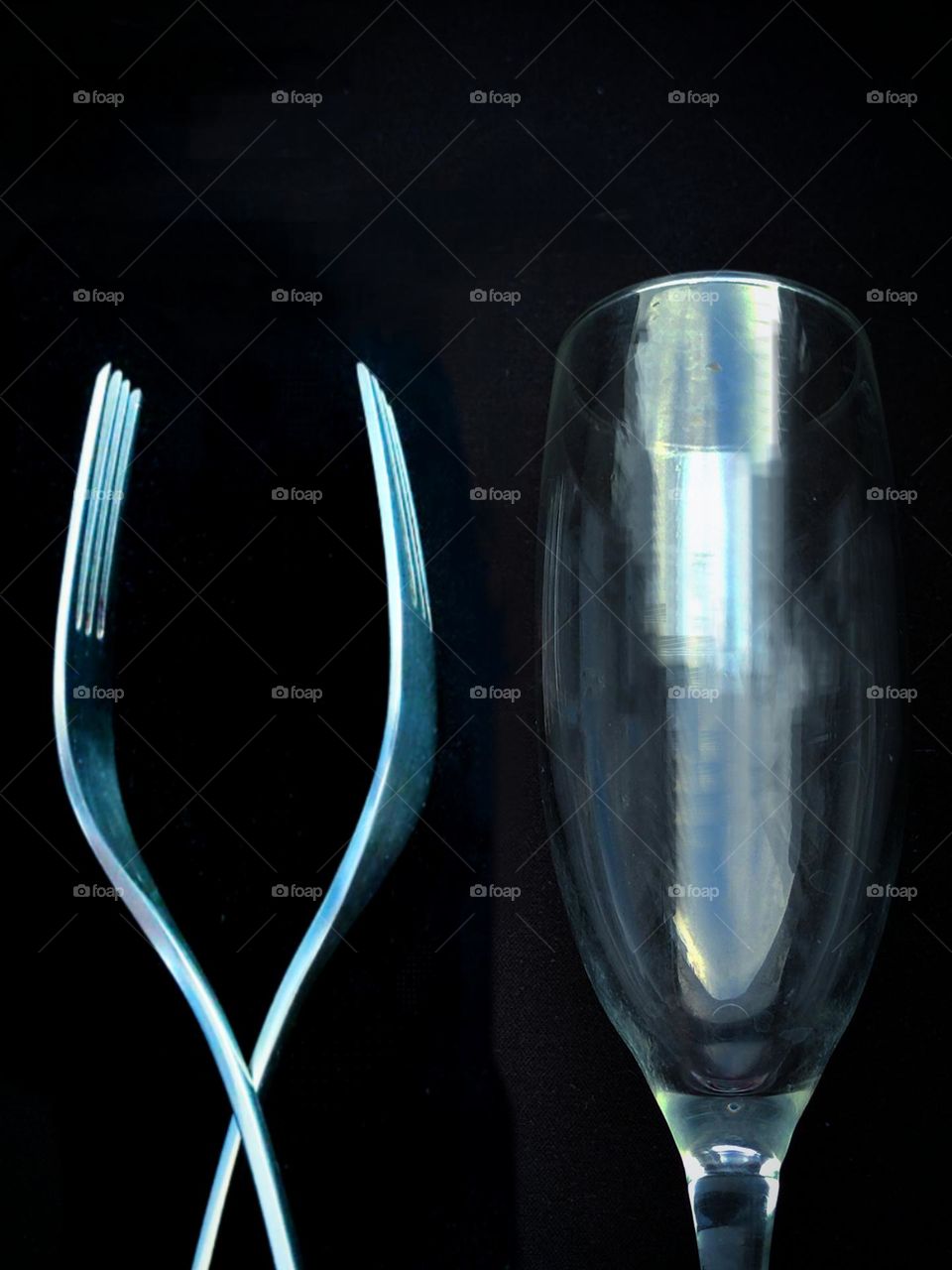 On a black background, two metal forks in the shape of a wine glass and a glass wine glass.