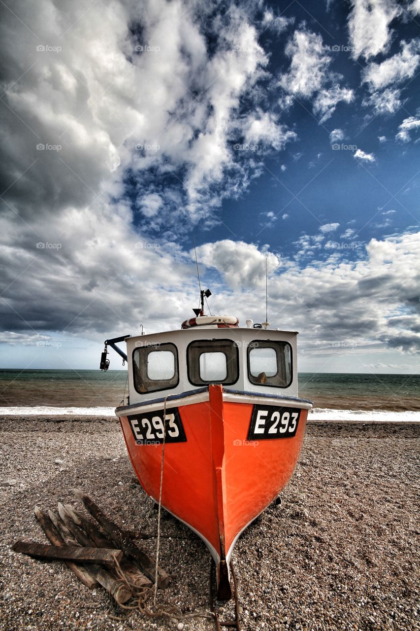 A beached fishing boat on a deserted pebble beach near the ocean.
