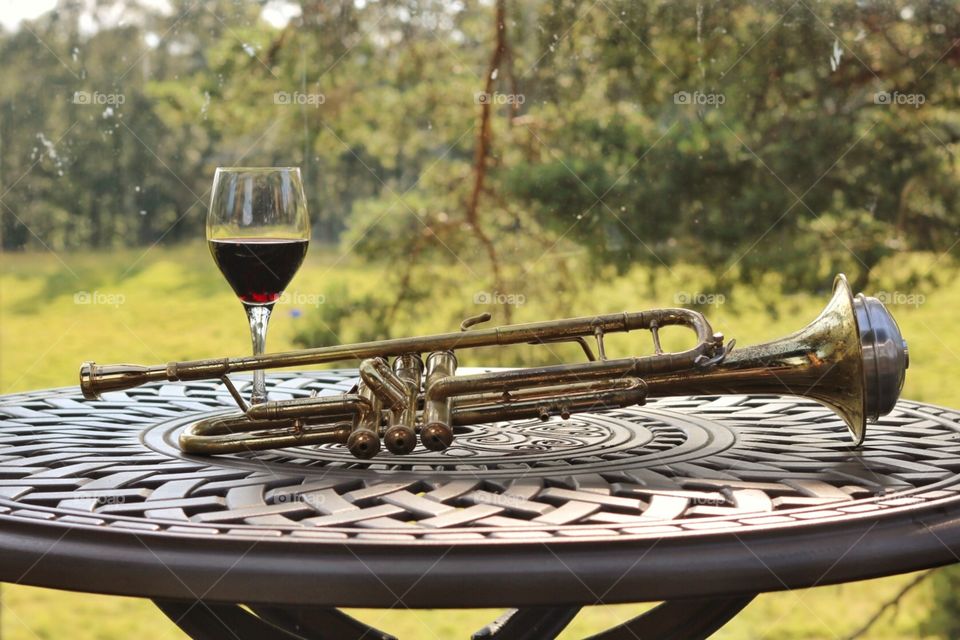 Table outside in the woods with a glass of red wine and a trumpet. 