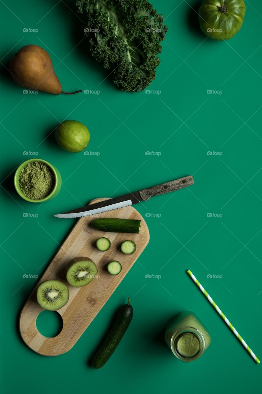Monochromatic green flat lay of green colored fruit and vegetable smoothie ingredients with a cutting board